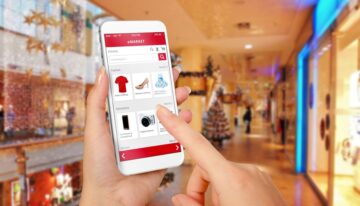 Smart phone online shopping in woman hand during Christmas. Shopping center in background. Buy clothes shoes accessories with e commerce web site